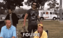 a group of people are standing in a park and one of them is holding a dog and the word fouine is on the screen .