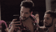 a man with a beard is looking at his cell phone in a crowded room .