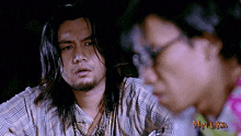 a man with long hair and a beard stands next to another man with glasses and the words may laksa on the bottom right