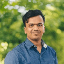 a man in a blue shirt is standing in front of a green background and smiling .