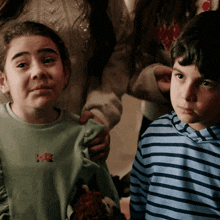 a girl wearing a green shirt with a flower on it is standing next to a boy wearing a blue striped shirt