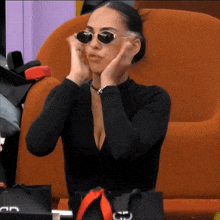 a woman wearing sunglasses is sitting in a chair with her hands on her ears