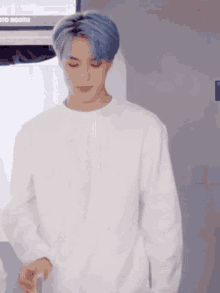 a young man with blue hair is wearing a white sweatshirt and standing in front of a photo booth .