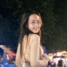 a woman wearing glasses and a tan shirt is smiling