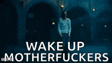 a man in a white shirt is standing in front of a building with the words `` wake up motherfuckers '' .