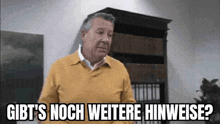 an older man in a yellow sweater is standing in front of a bookshelf and making a funny face .