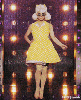 a woman in a yellow and white polka dot dress is standing on a stage