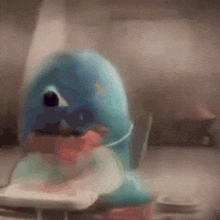 a blue stuffed animal is sitting on a table with a remote control in its mouth .