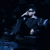 a man sitting in a chair smoking a cigarette and wearing sunglasses