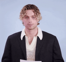 a man with curly hair is wearing a black jacket and a white shirt