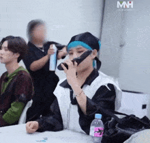 a man is sitting at a table with a bottle of water in front of him and a sign that says mh on it