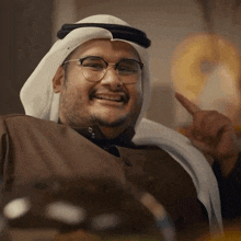 a man wearing glasses and a head scarf is pointing up