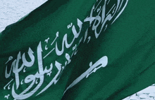 a green and white flag with arabic writing waves in the wind