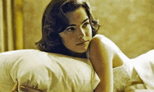 a woman is laying on a bed holding a pillow and looking at the camera .