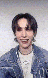a young man wearing a denim jacket and headphones is smiling and making a funny face .
