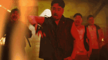 a group of men are standing in a dark room with red lights behind them
