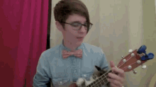 a man wearing glasses and a bow tie is playing an ukulele .