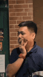 a man in a blue shirt and red watch is covering his mouth with his hand .