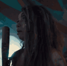a woman with dreadlocks is holding a wooden stick with a sticker on it that says ' a.k. '