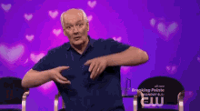 a man in a blue shirt is sitting in front of a purple background with hearts
