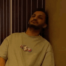 a man with a beard is leaning against a wall wearing a t-shirt with a logo on it .
