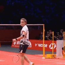 a person holding a badminton racket on a court with a sign that says victor
