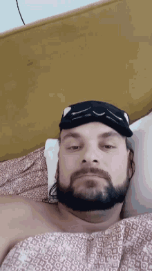 a man with a beard is laying on a bed with a black mask on his face