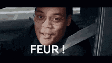 a man wearing glasses is sitting in a car with a seat belt on .