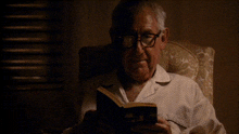 a man wearing glasses is reading a book in a dark room
