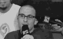 a man wearing glasses is speaking into a microphone .