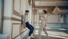 a man leans against a wall while a woman dances in an empty room