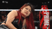 a woman with red hair is in a wrestling ring with a bottle of prime in the background
