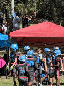 a group of young football players are huddled under a red tent