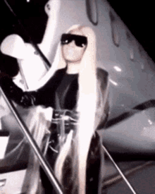 a woman with long blonde hair wearing sunglasses is standing next to a plane .