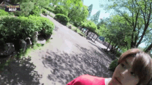 a person in a red sweater is walking down a path in a park with trees and bushes .
