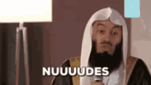 a man with a beard and a robe is holding a microphone and saying nuuuudes .