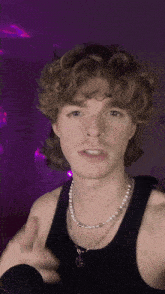 a young man with curly hair wearing a black tank top and a pearl necklace .