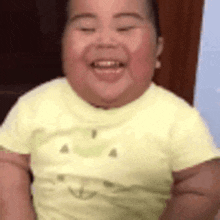 a baby in a yellow shirt is smiling for the camera .