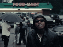 a man wearing a hooded jacket stands in front of a food mart