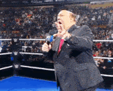 a man in a suit is holding a microphone in front of a wrestling ring
