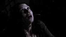 a woman with blood on her face is screaming in the dark with her mouth wide open .