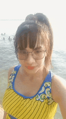 a woman wearing glasses and a yellow and blue striped tank top is taking a selfie in the water
