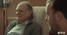 an older man sits in a chair talking to another man with netflix written on the bottom right