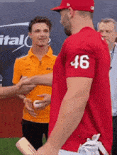 a man in a red shirt with the number 46 on the sleeve shakes hands with another man