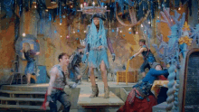 a woman in a blue dress is standing on a stage surrounded by other people