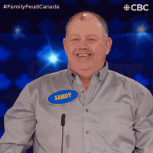 a man with a name tag that says sandy stands in front of a microphone