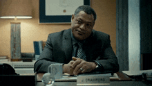 a man in a suit and tie sits at a desk with a name tag that says j crawford