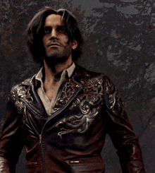 a man in a brown leather jacket stands in front of a forest