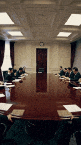 a group of men are sitting around a large wooden table in a conference room