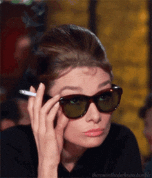 a woman wearing sunglasses holds a cigarette in her hand